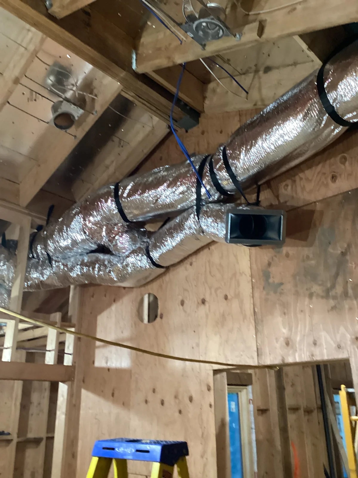 Insulated flex duct supply runs with a sheet metal register boot strapped to plywood framing during an attic ductwork install in the High Desert.