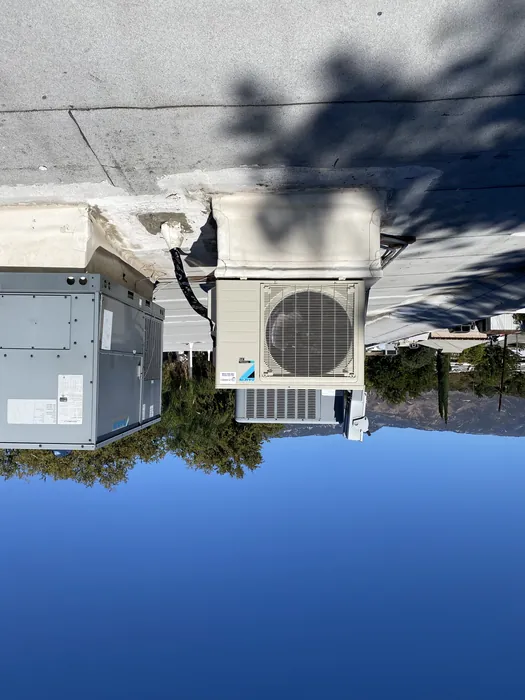 Daikin mini-split condenser set on a roof pad next to a larger rooftop package unit under clear High Desert sky.