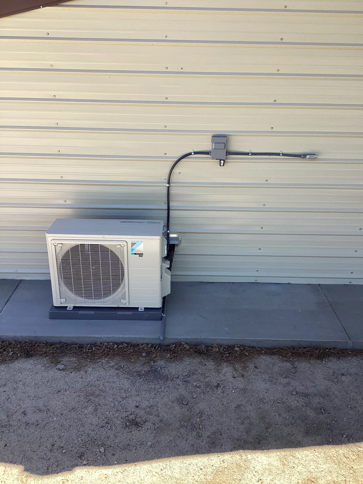 Daikin mini-split outdoor unit with electrical disconnect box and line set neatly run down a metal building wall in the Inland Empire.