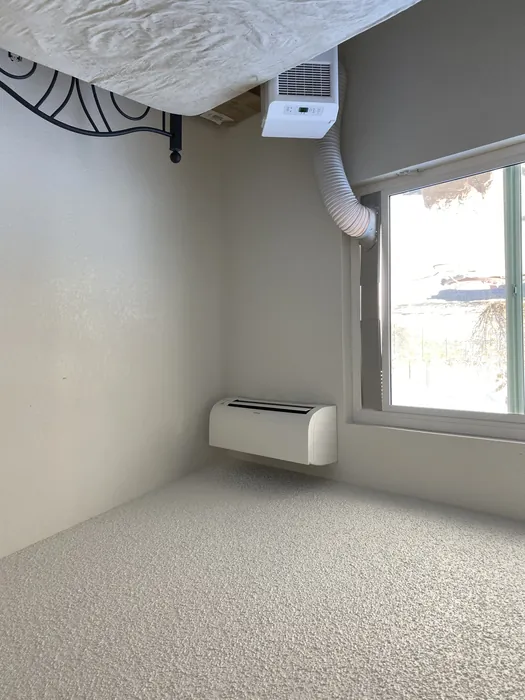 Indoor mini split wall head newly installed in a bedroom alongside an older window AC unit being replaced.