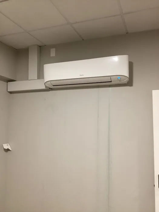 A white ductless mini-split indoor air handler head mounted high on a wall above light tile in an indoor room.