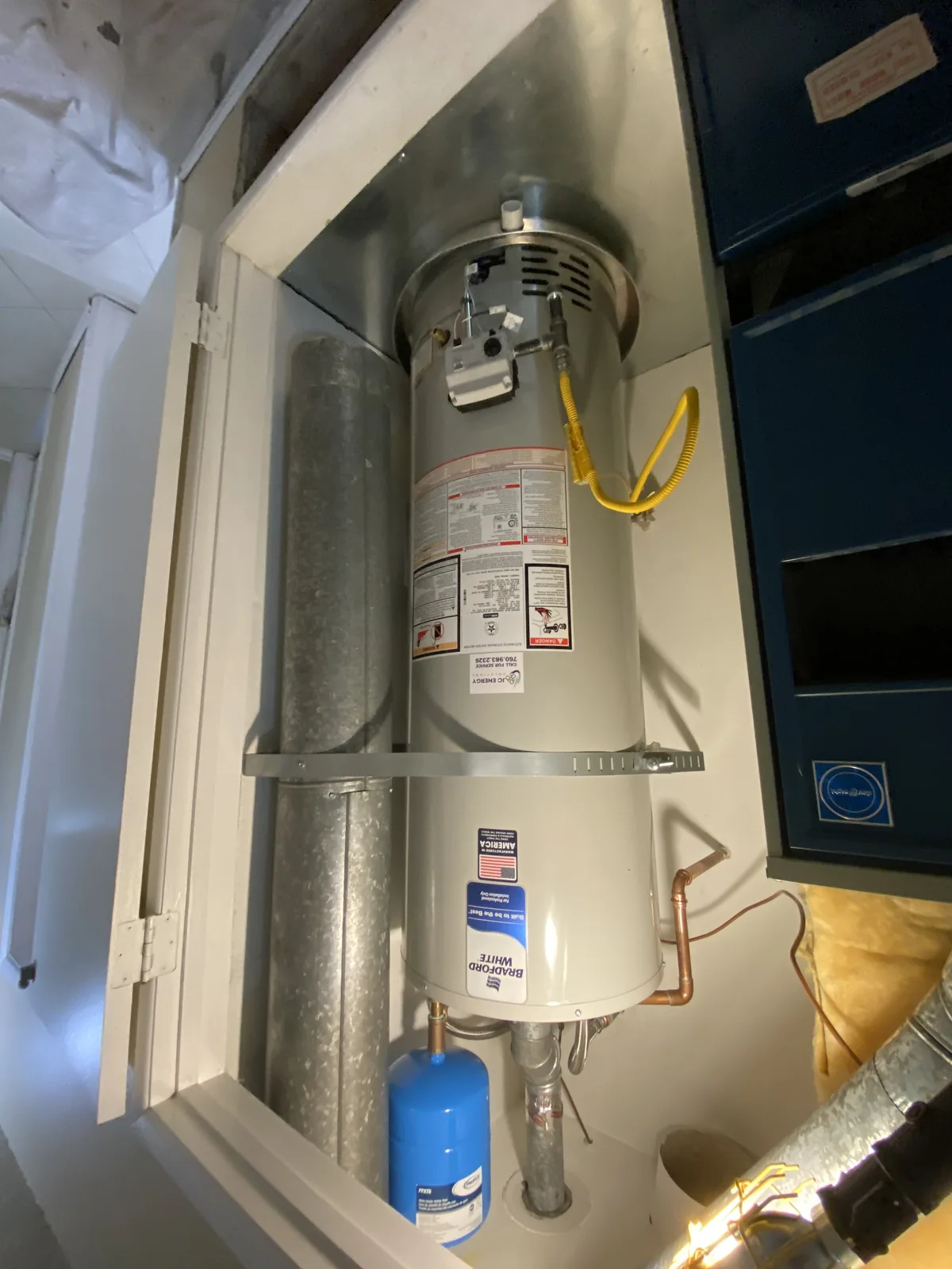Bradford White gas water heater with a JC Energy sticker, expansion tank and gas connector installed in a utility closet.